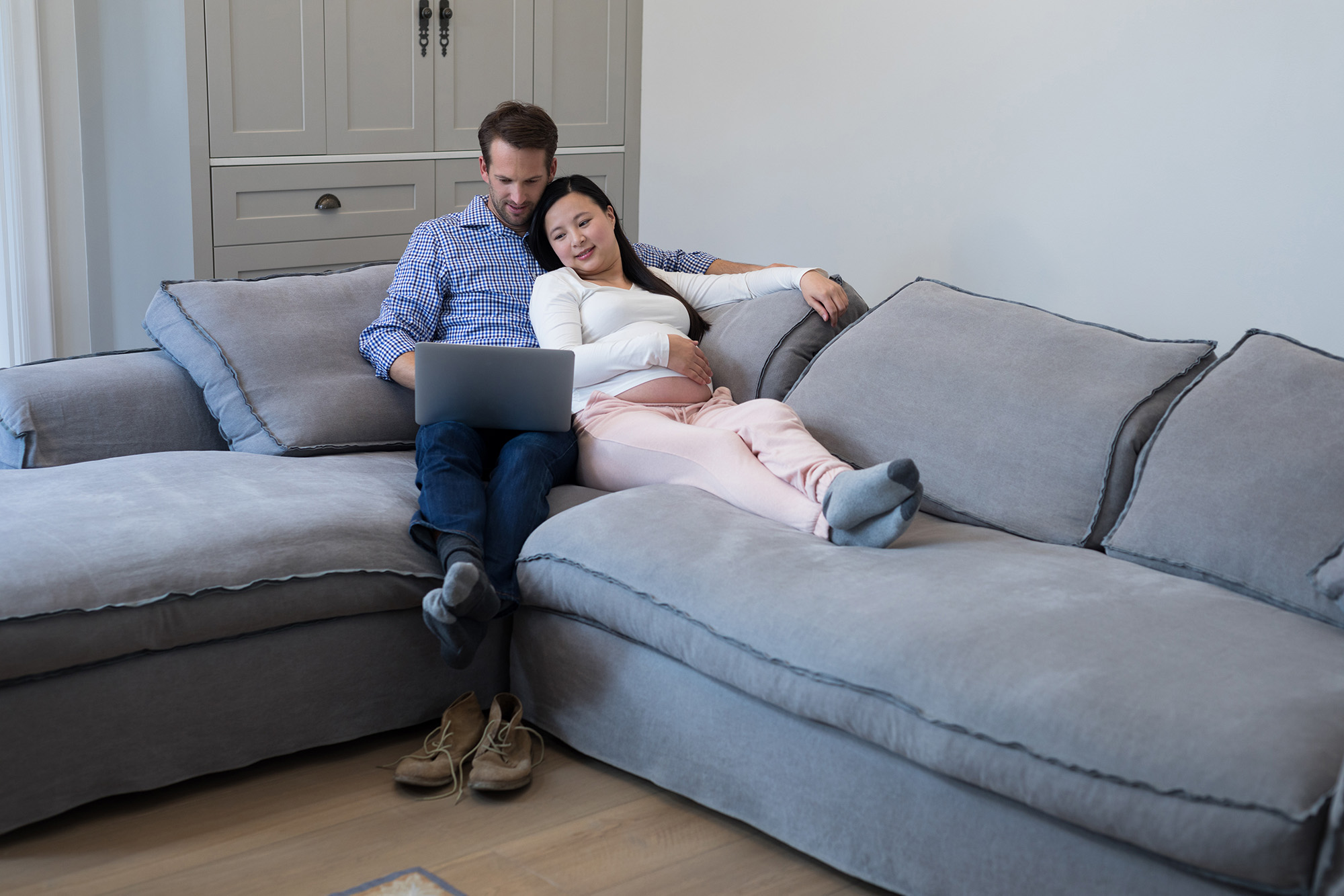 Heterosexual couple watching something on a tablet while smiling. They are sitting on a couch and he's hugging her from behind.
