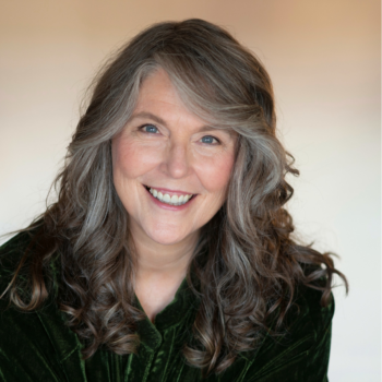 Portrait of Tracy Adams. Tracy is smiling at the camera. She is wearing black framed glasses and a blue and white stripped shirt.